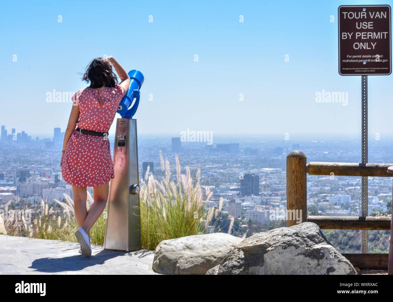 Señora recostada sobre telescopio en las colinas de Hollywood con el horizonte de Los Angeles en la distancia Foto de stock