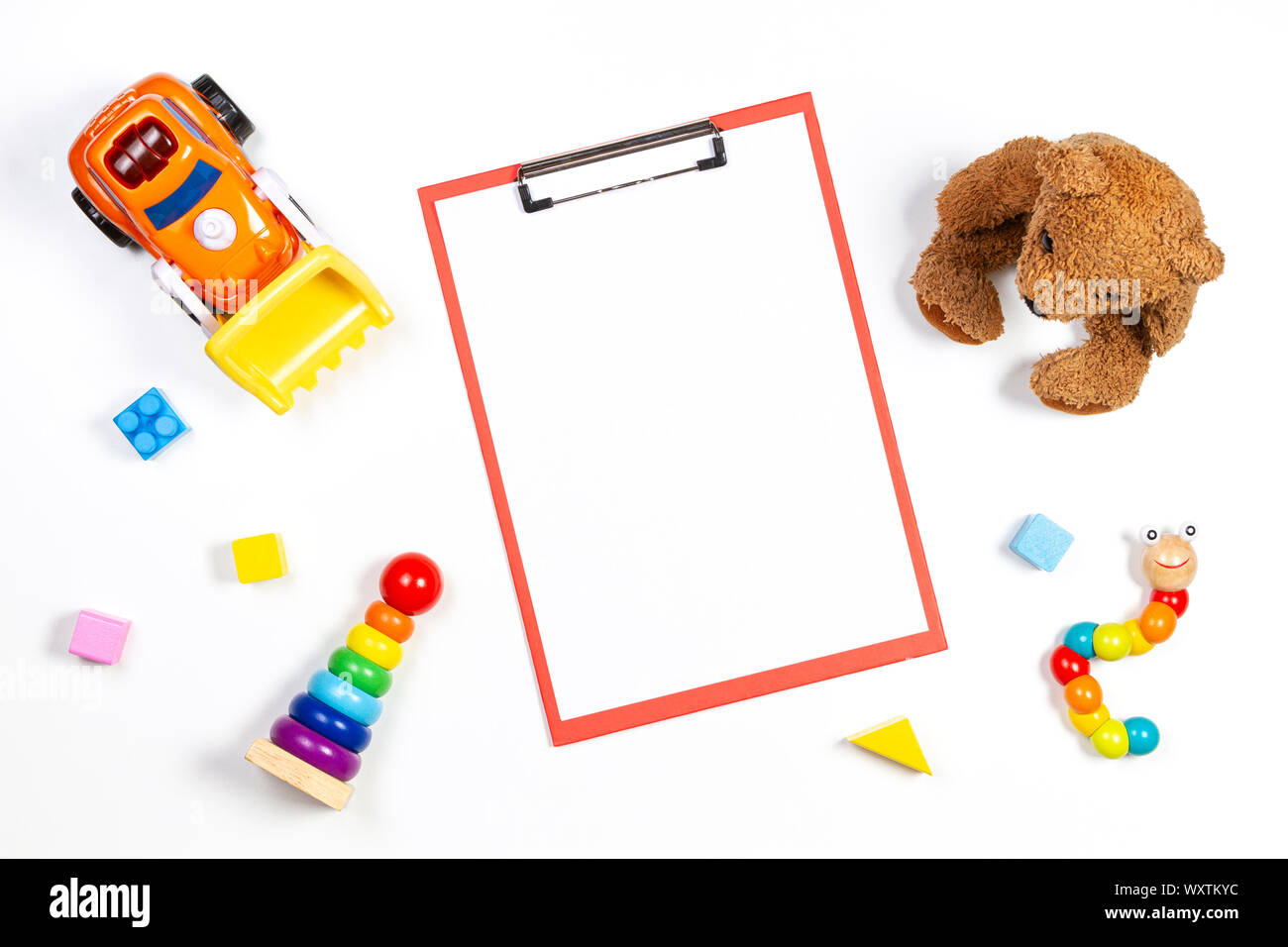 Colorido bebé juguetes kid y red portapapeles con hoja de papel en blanco sobre fondo blanco. Vista superior Foto de stock