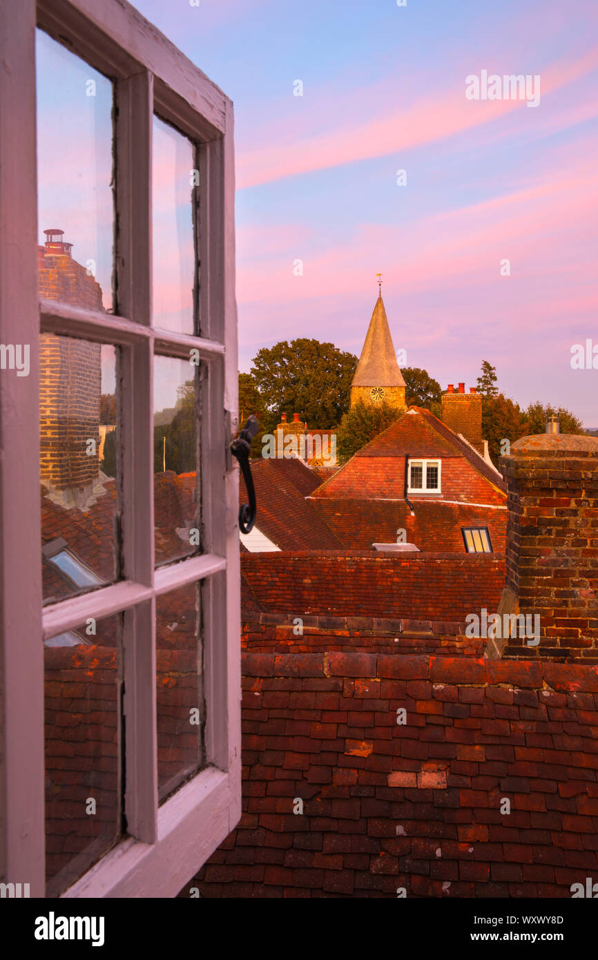 Vista a través de la ventana abierta por los tejados de Burwash a la iglesia de San Bartolomé al atardecer, Burwash, East Sussex, Inglaterra, Reino Unido, Europa Foto de stock