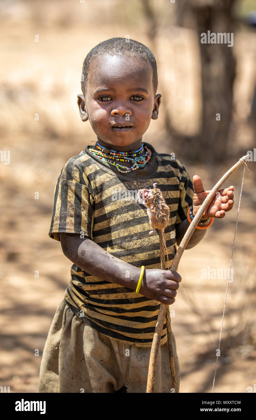 El lago Eyasi, Tanzania, 11 de septiembre de 2019: Hadzabe kid con un arco y flechas y un pequeño ratón que ha pescado Foto de stock