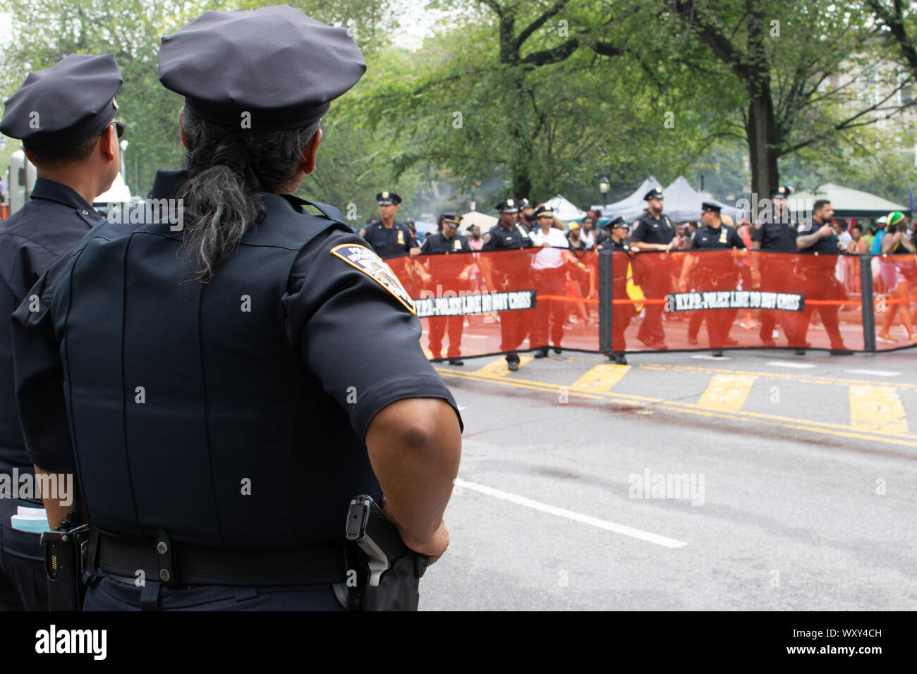Enlaces stehen Polizisten, am Rander der Parade, in der Mitte sieht man Polizisten, die vor einem Wagen laufen, der auf der West Indian Day Parade en ne Foto de stock