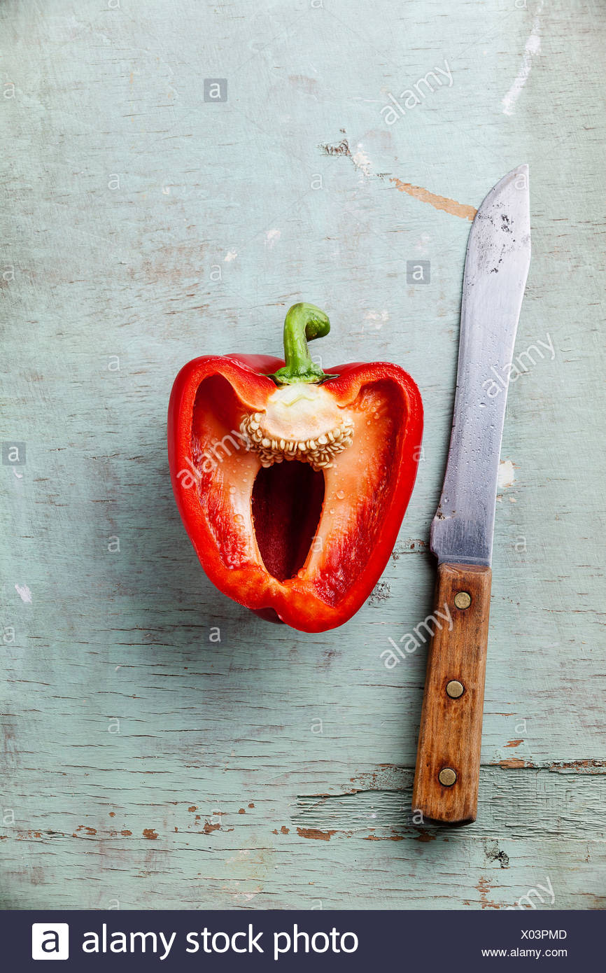 La mitad del pimiento rojo y el cuchillo en la textura de fondo azul Foto de stock