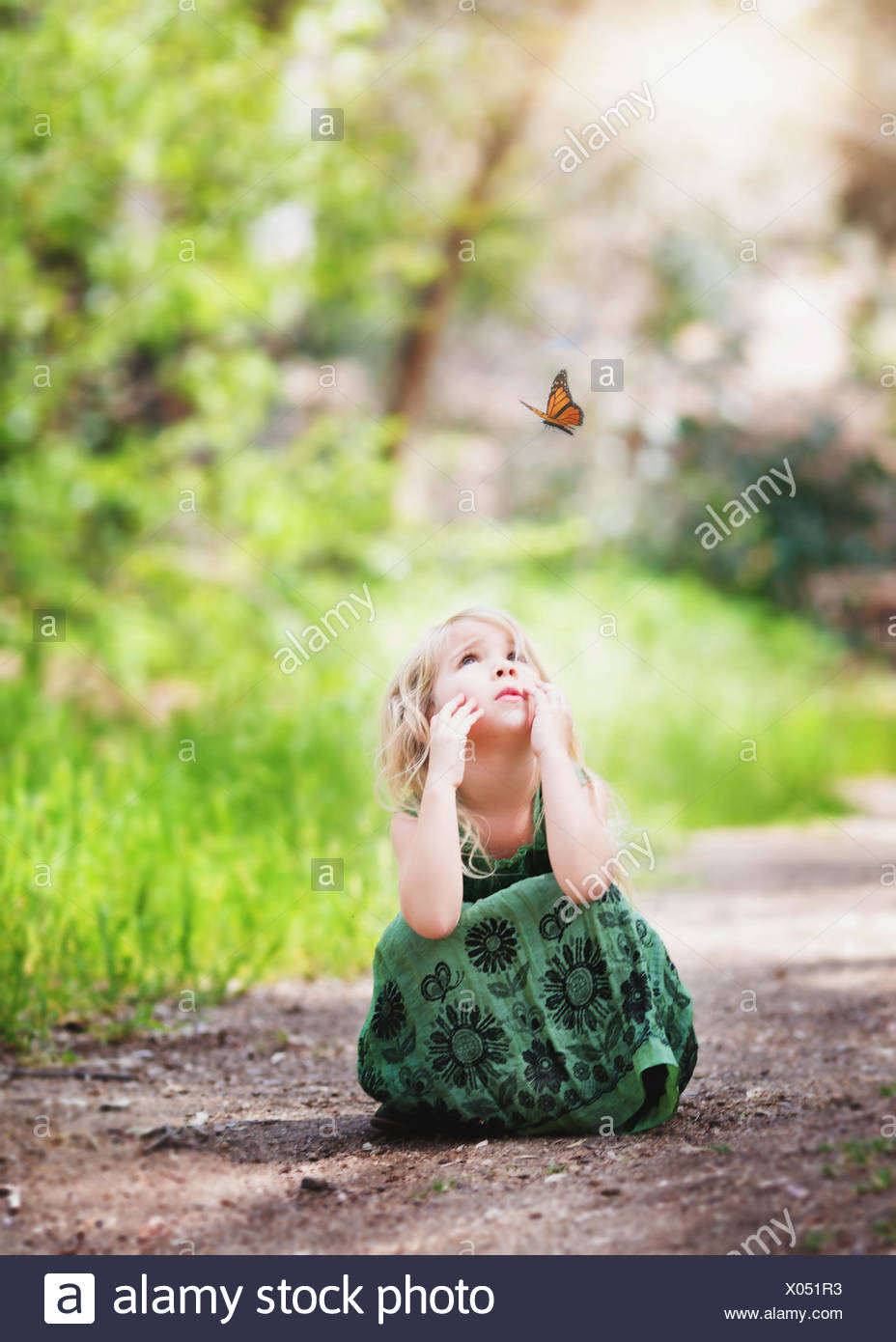 Niña sentada en un camino mirando a una mariposa, California, EE.UU Foto de stock