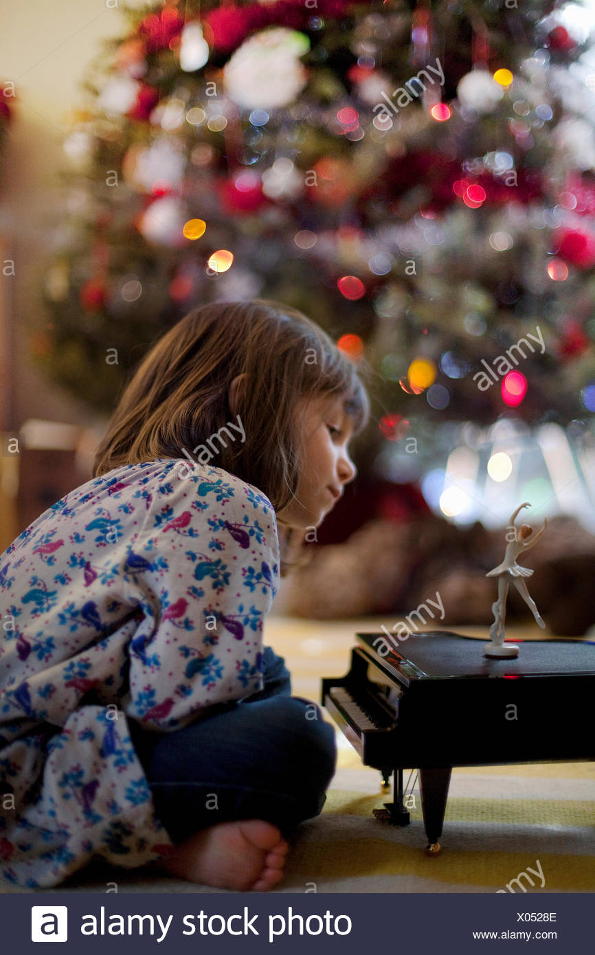Chica sentada en el suelo del cuarto de estar escuchando música de piano de juguete en Navidad caja Foto de stock