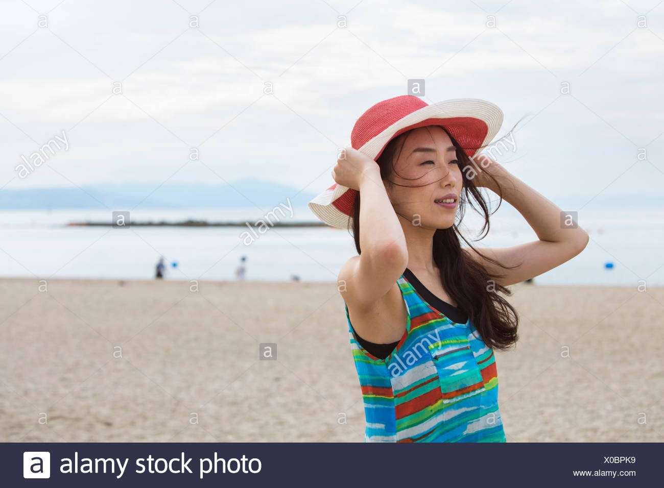 Una mujer en una playa en Kobe, sosteniendo su sombrero. Foto de stock