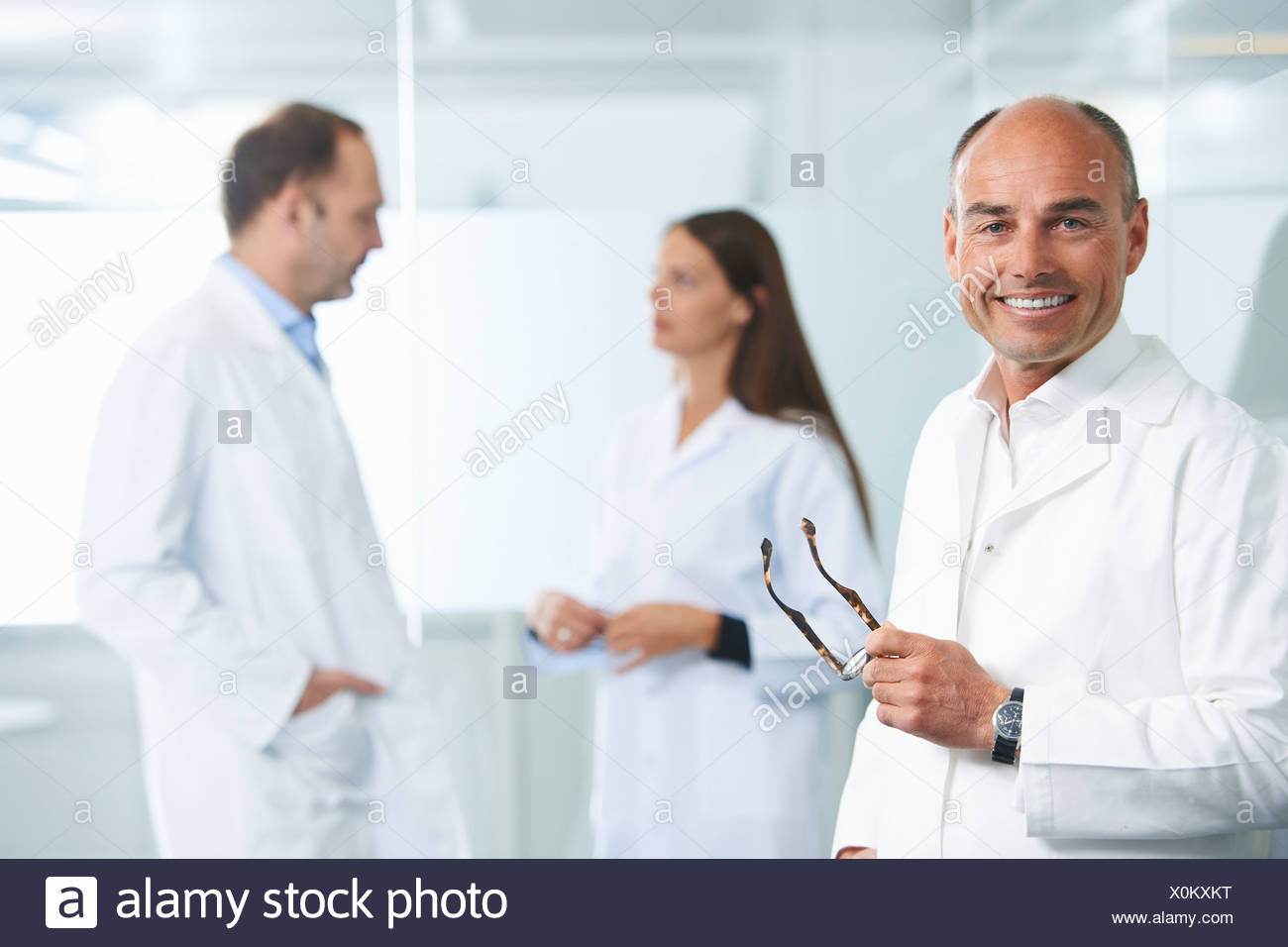 Médico varón por pared reflectante, colegas en segundo plano. Foto de stock