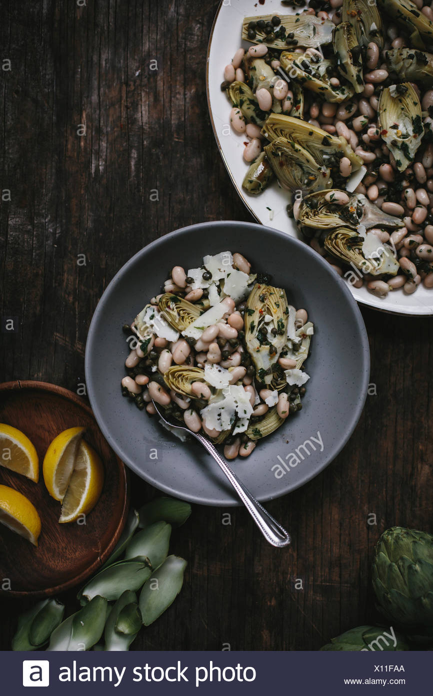 Una taza de Ensalada de alcachofas bebé braseada con judías blancas y rasura manchego es fotografiado desde la parte superior. Foto de stock