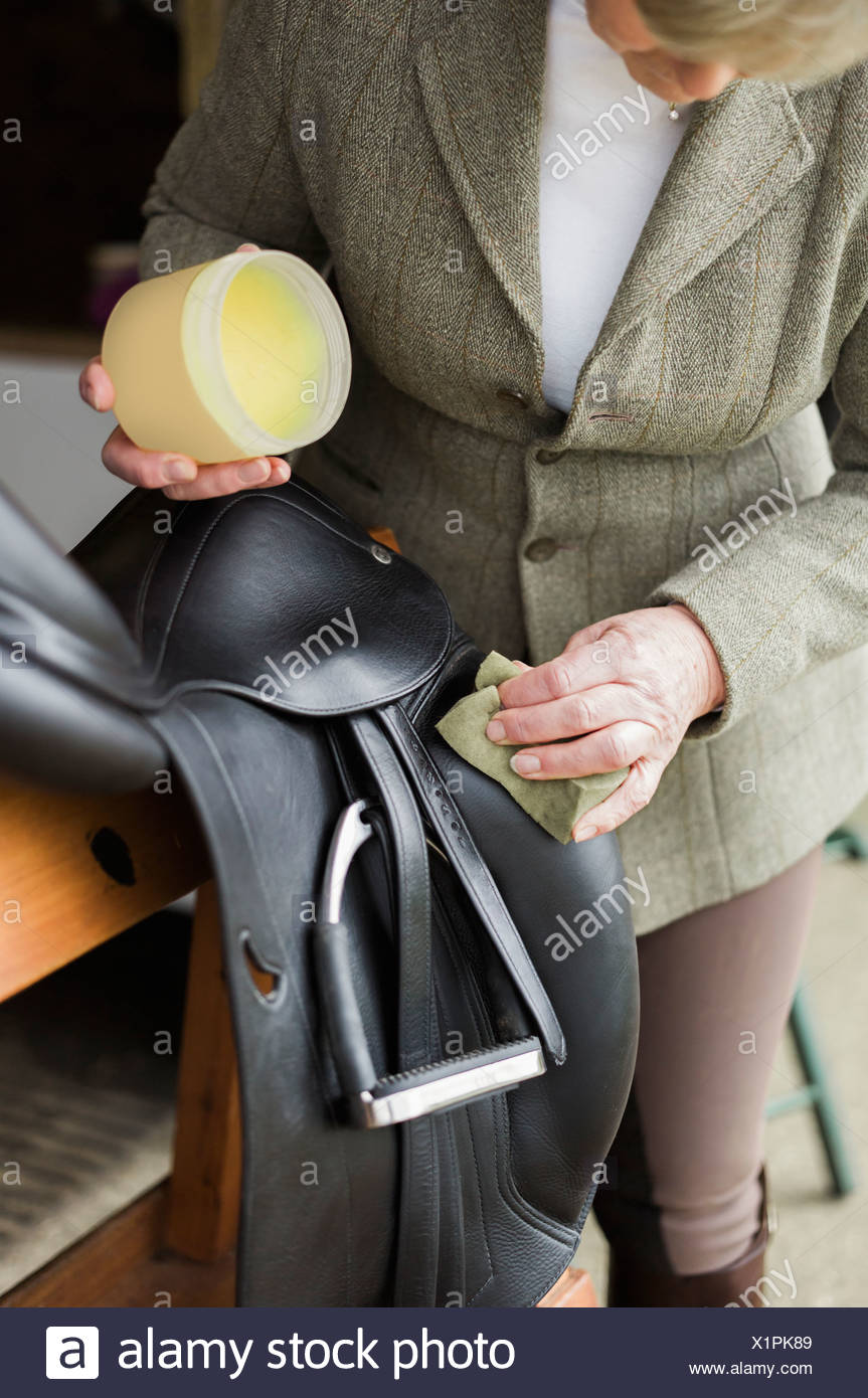 Una mujer de limpieza y preparación de tack y sillín en el patio de una caballeriza. Foto de stock