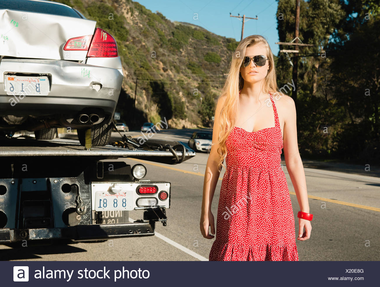 Mujer joven mirando a la cámara como Tow Truck quita auto dañado Foto de stock