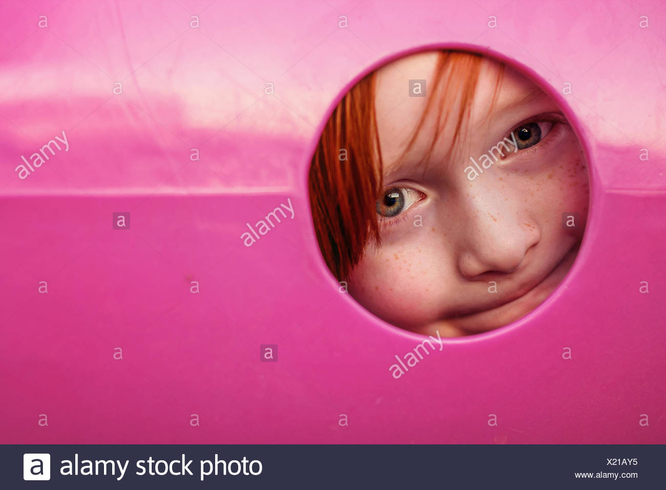 Joven peeking a través del agujero en el túnel de recreo Foto de stock