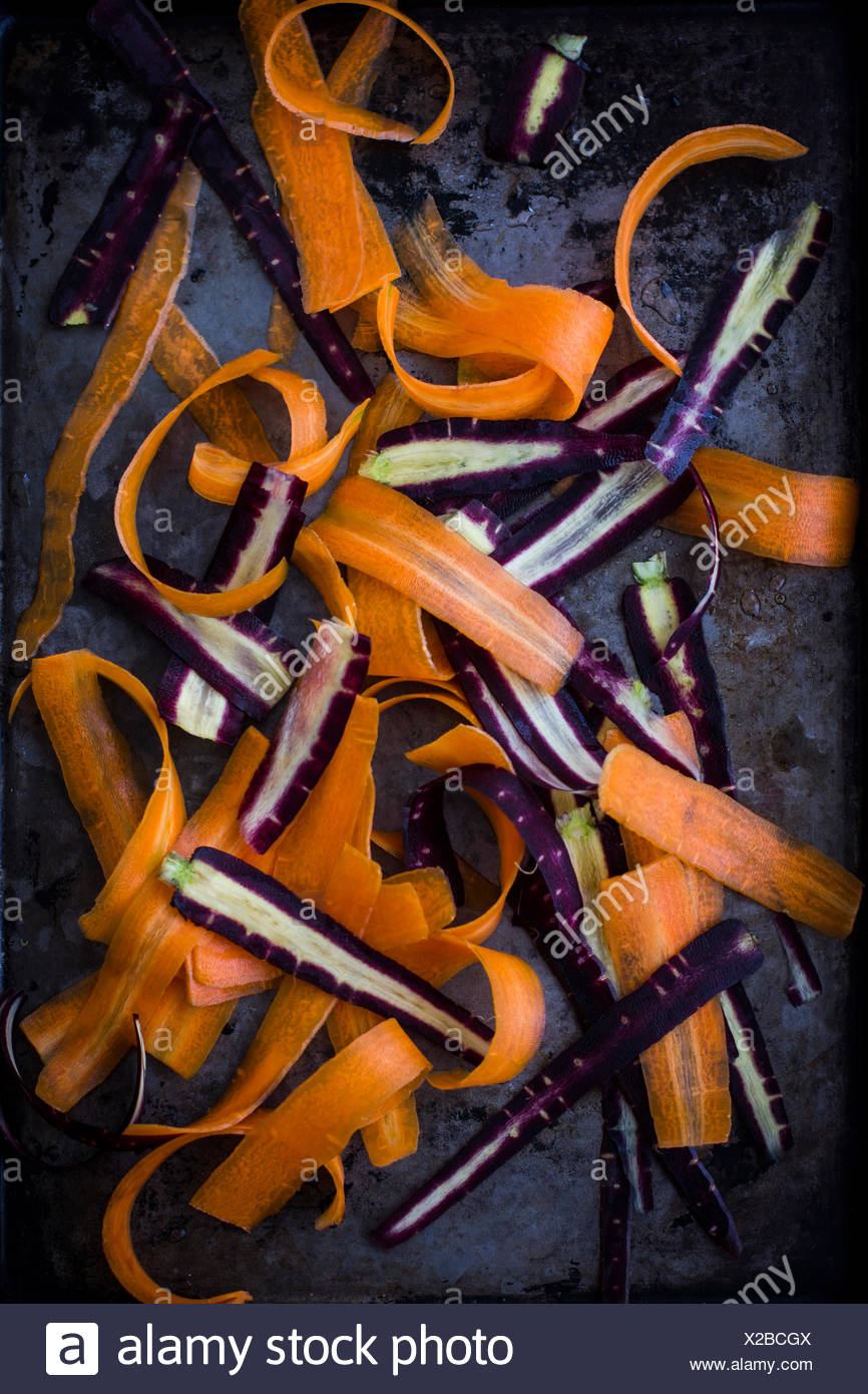 Morado y naranja zanahorias, afeitado, en bandeja oscura Foto de stock
