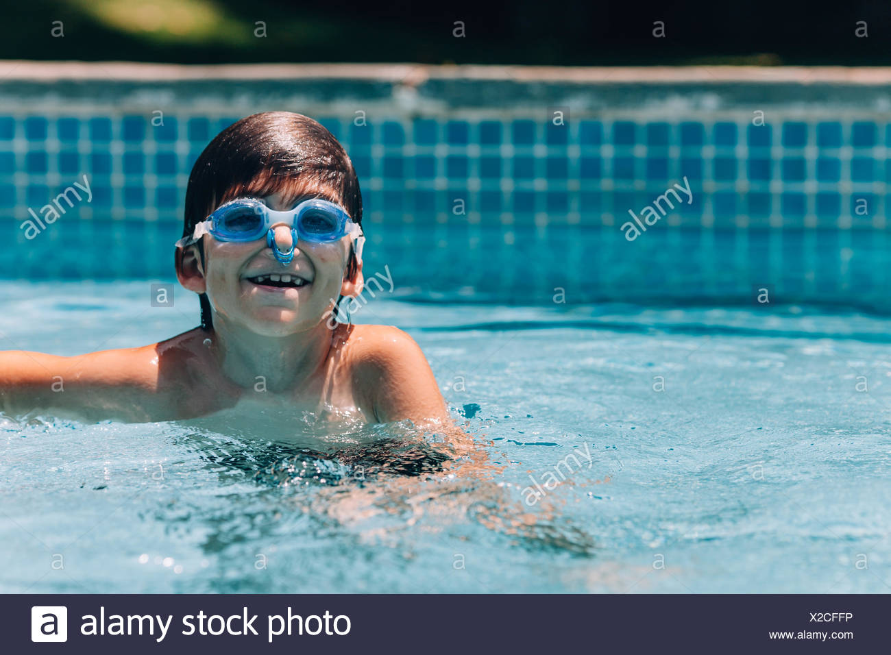 Chico sonriente gafas protectoras y pinza para nariz en piscina Foto de stock