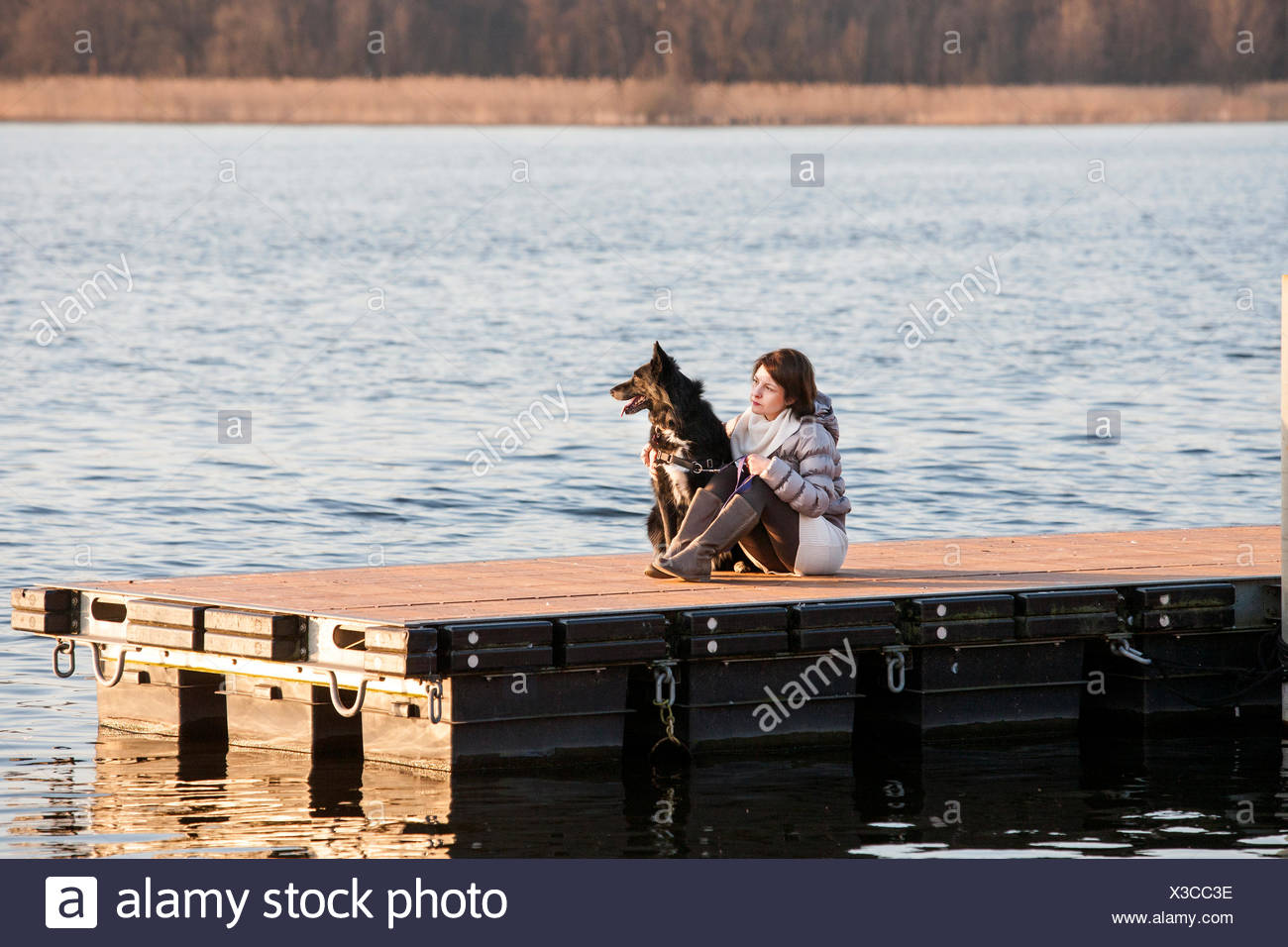 Mitad mujer adulta y su perro sentado en el lago pier Foto de stock