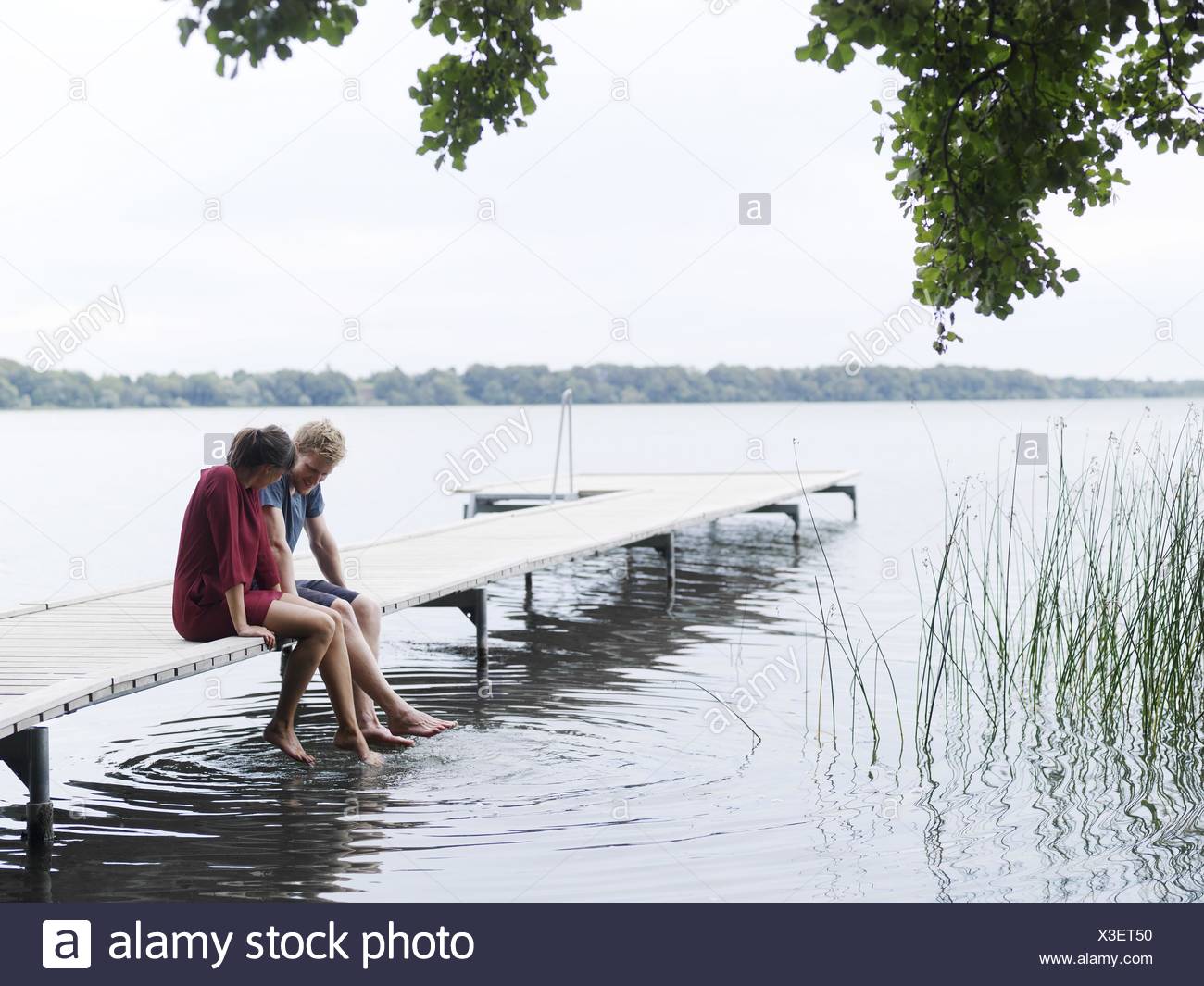 Pareja Sentada en el muelle al lado sumergir los pies en agua, Copenhague, Dinamarca Foto de stock