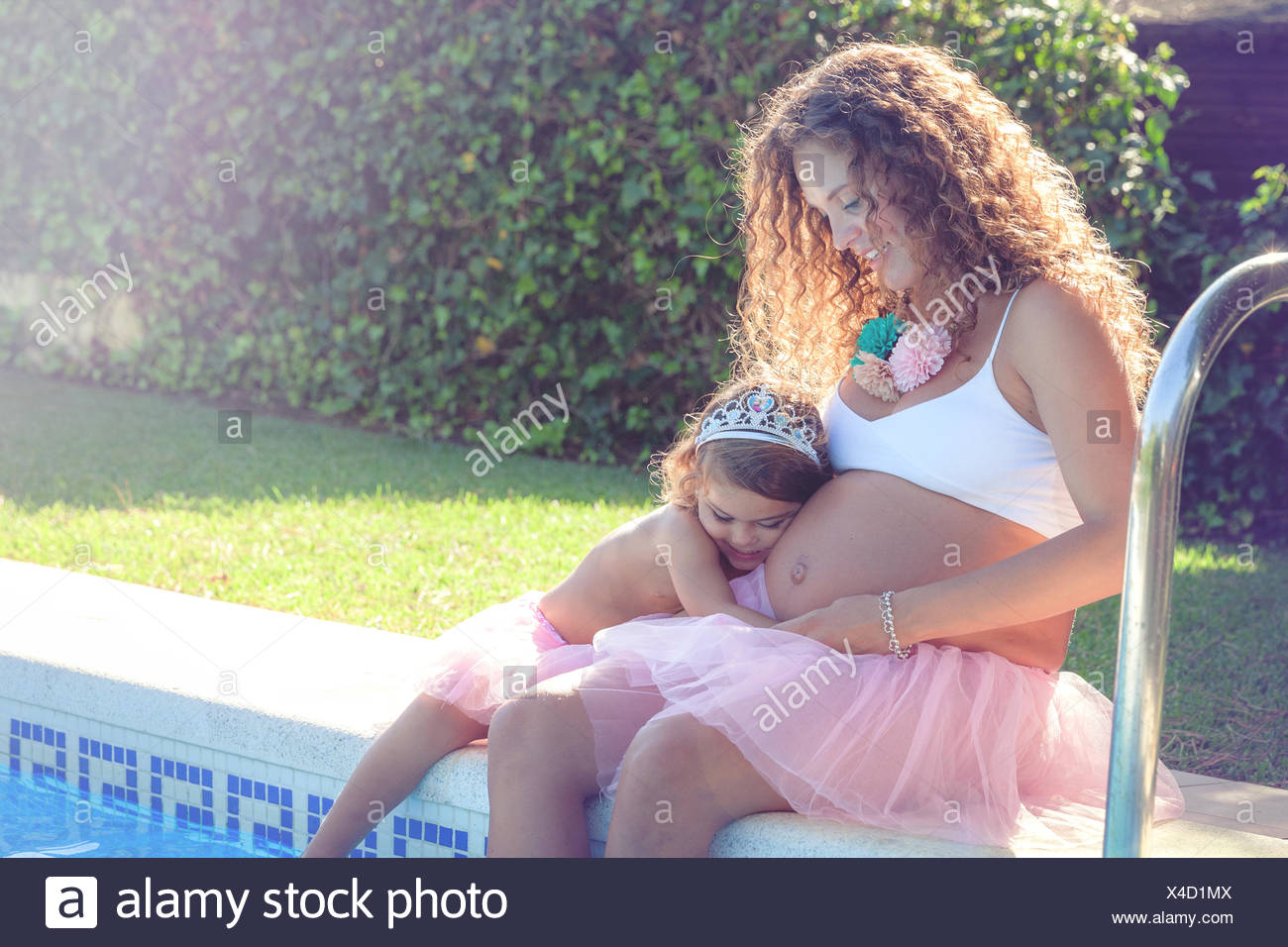 Mujer embarazada sentada con mi hija por piscina Foto de stock