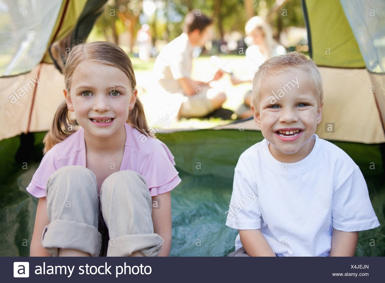 Una feliz pareja de chicos sentarse en el interior de la carpa mientras sus padres están fuera Foto de stock