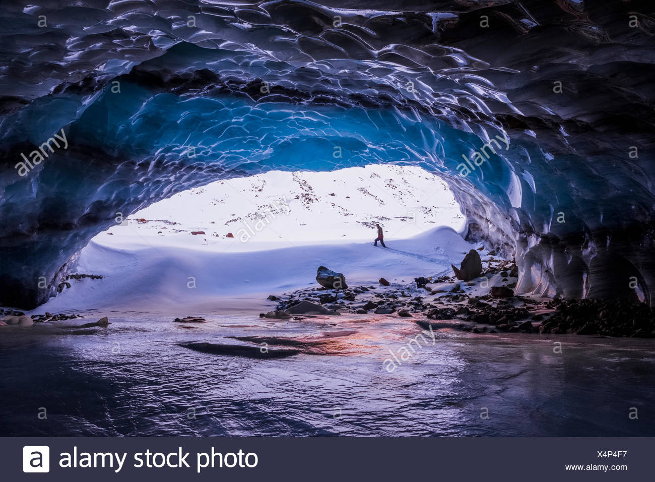 Un hombre está enmarcada por la entrada de una gran cueva de hielo cerca de la terminal de Augustana glaciar en la Cordillera de Alaska en invierno Foto de stock