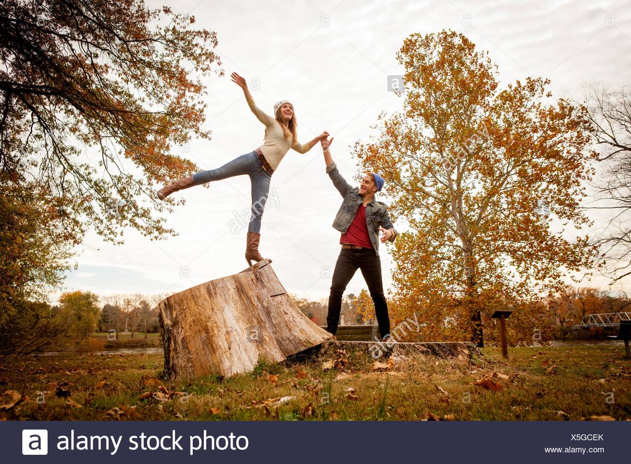 Pareja joven jugando en tocón de árbol en otoño park Foto de stock