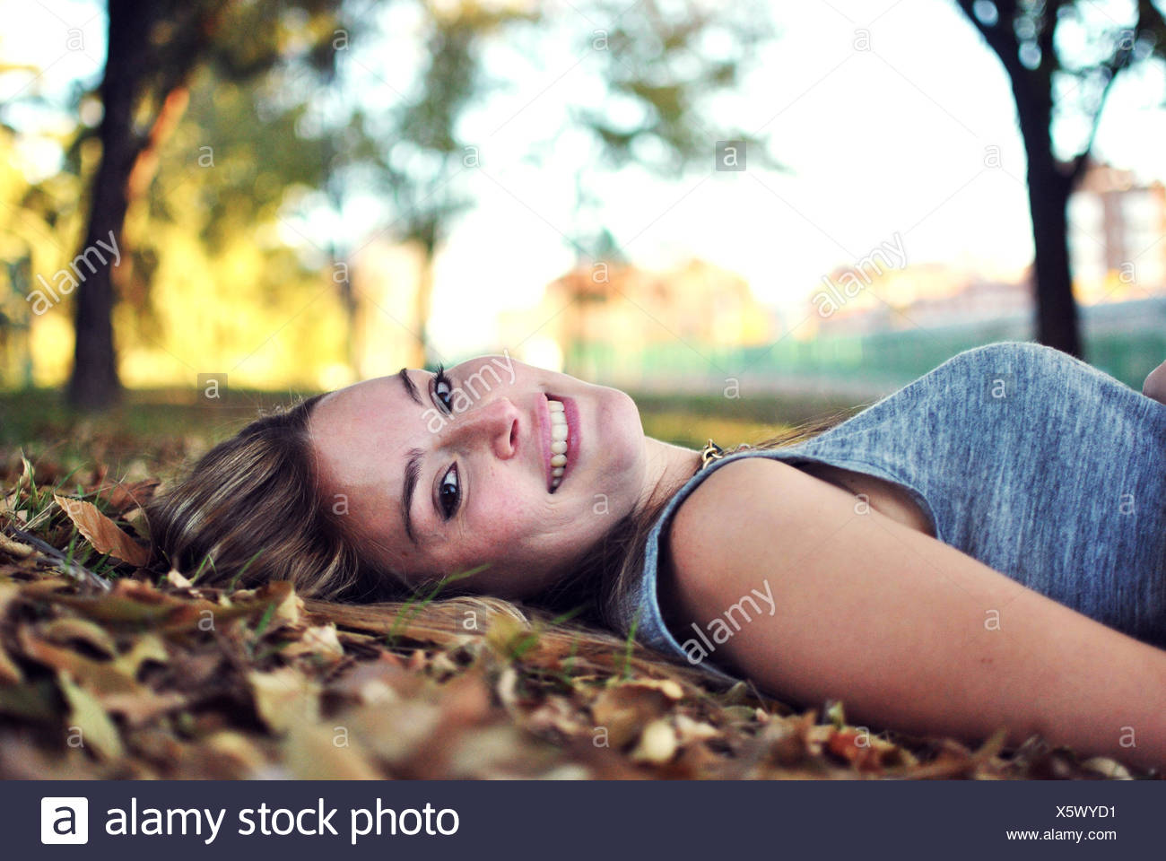 Retrato de mujer sonriente tumbado sobre hojas de otoño Foto de stock