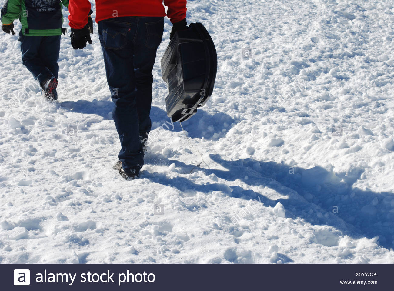 Niño de 7 lleva su trineo back up la ladera de montaña cubiertas de nieve Foto de stock