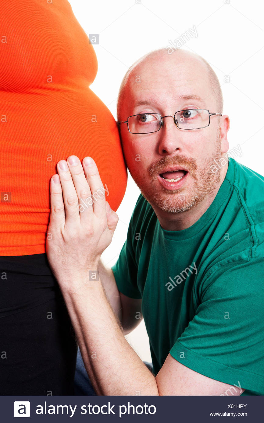 Hombre maduro, escuchando a la mujer embarazada la barriga contra el fondo blanco. Foto de stock