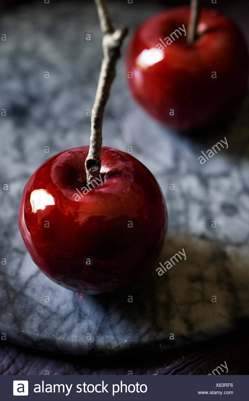 Detalle de la filmación, rojo brillante manzana de caramelo con twig stick en una bandeja de mármol oscuro, Moody sentir. Foto de stock