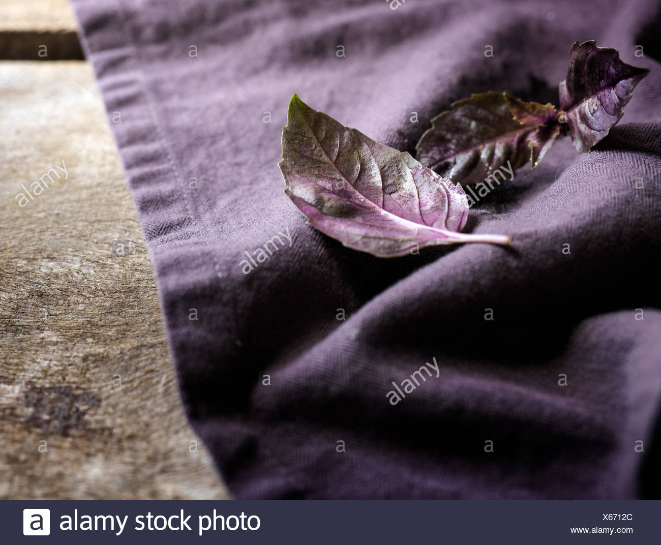 Detalle shot de hojas de albahaca morada en una ropa de color purpura y superficie de madera rústica. Foto de stock
