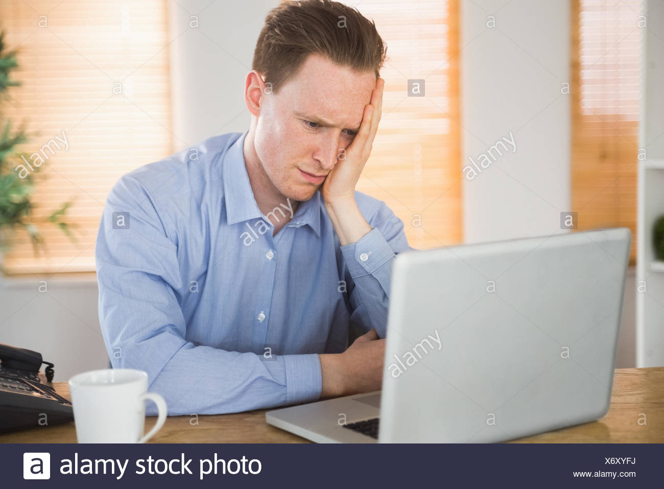 Empresario temeroso mirando a su portátil. Foto de stock