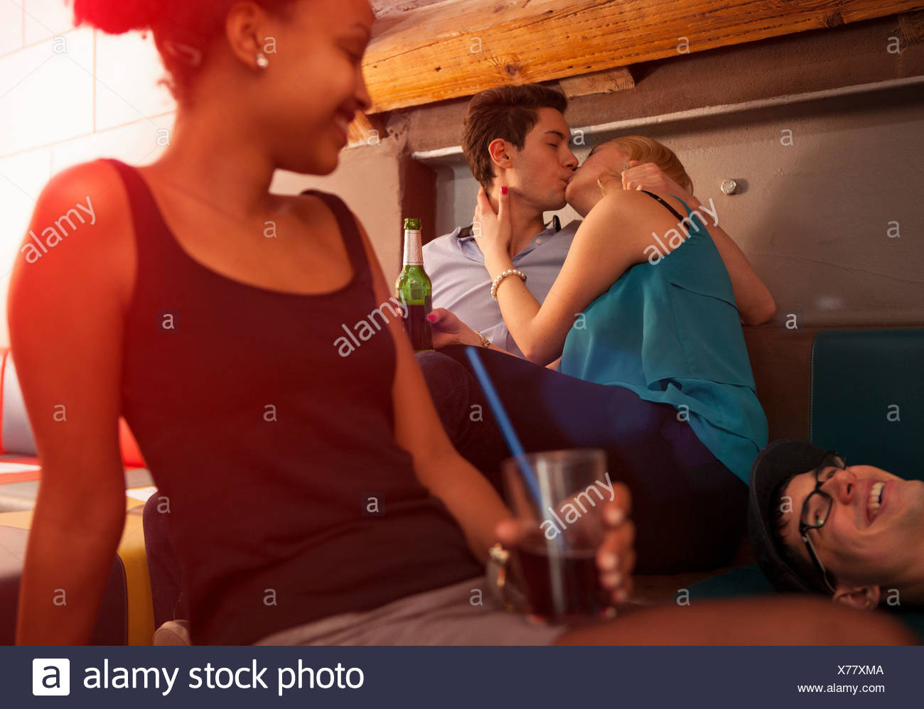 Joven pareja besándose, amigos sentado cerca Foto de stock