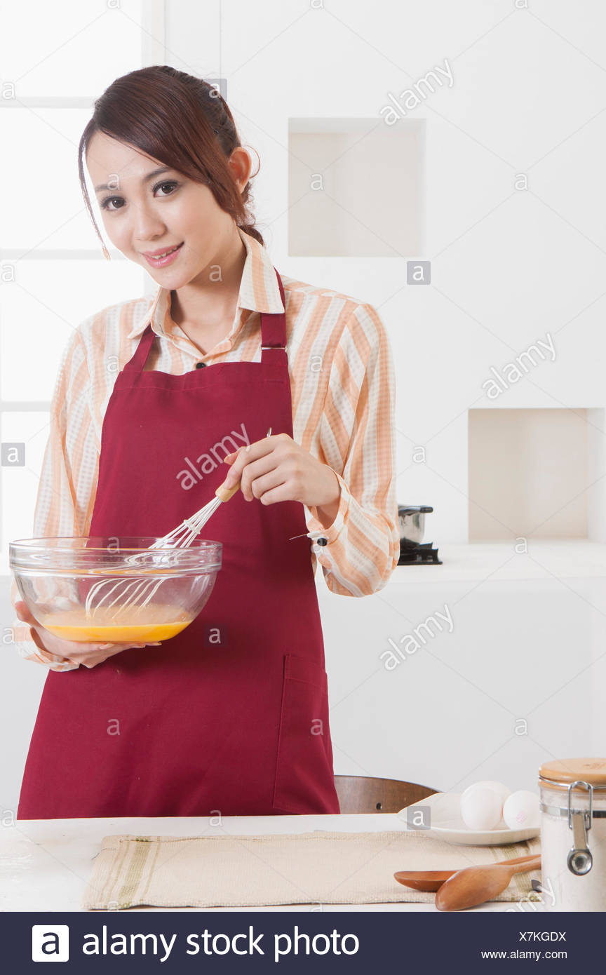 Mujer joven sujetando el cable batidor de huevos y sonriendo a la cámara. Foto de stock