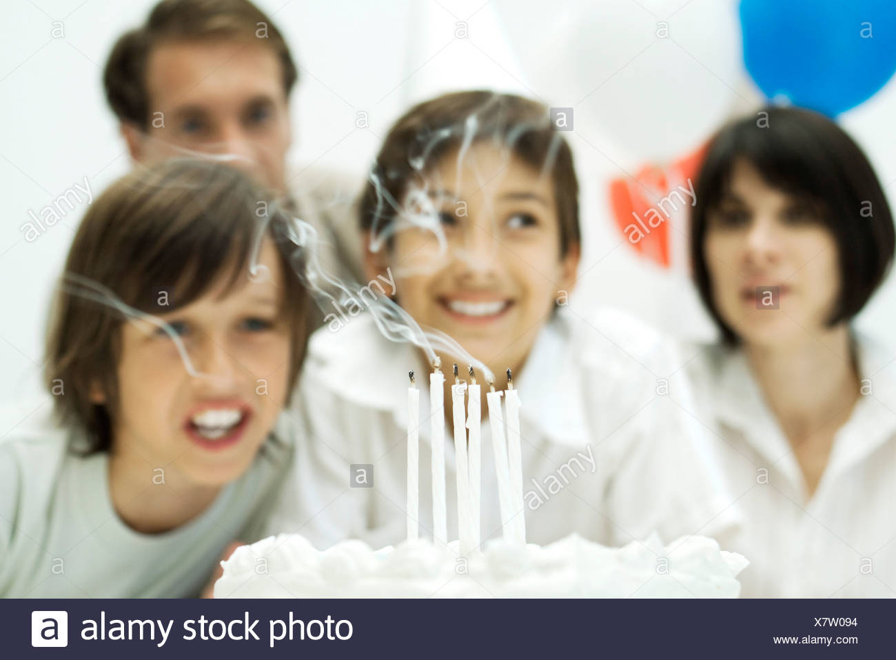 Los niños soplar las velas en el pastel de cumpleaños, los padres en segundo plano. Foto de stock