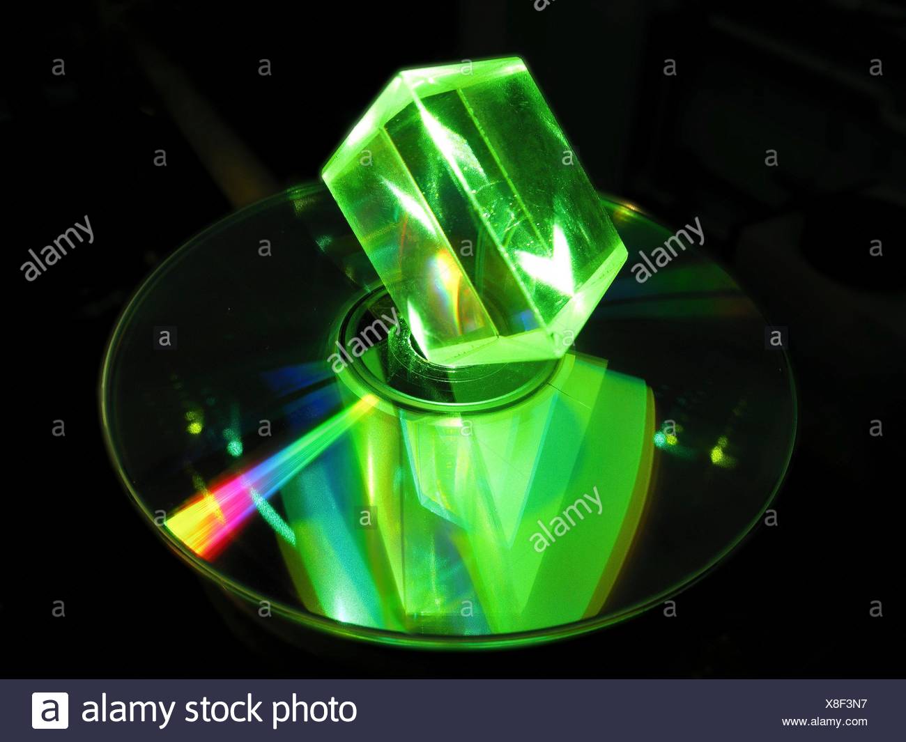 Prisma de vidrio y láser. Prisma de vidrio iluminado con luz láser verde, con un reflejo visto en un disco óptico. Discos compactos (CD) y los discos versátiles digitales (DVD) son ejemplos de discos ópticos. Prismas de vidrio óptico son dispositivos utilizados para refractar y di Foto de stock