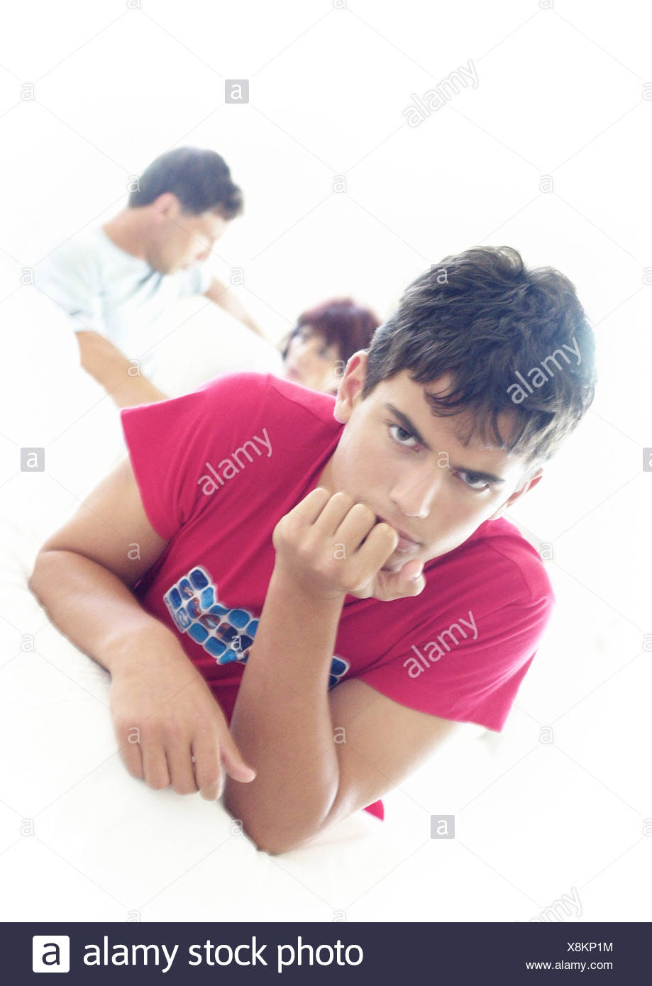 Joven con la mano bajo el mentón, padres hablando en segundo plano. Foto de stock