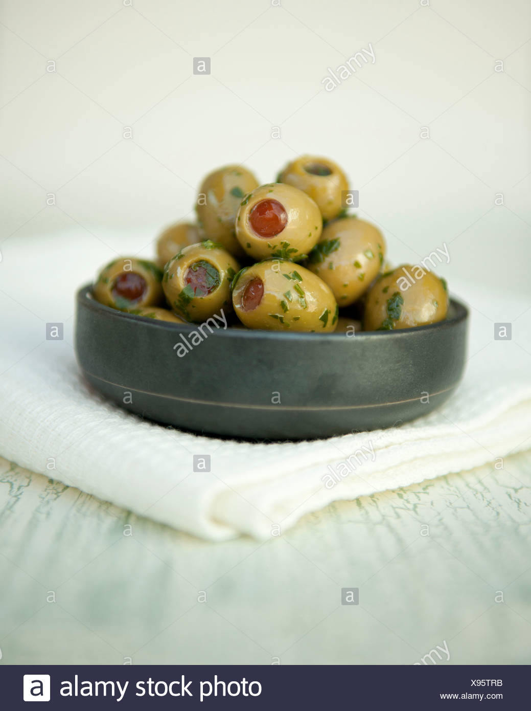 Aceitunas verdes rellenas con pimientos rojos con aceite de oliva y las hierbas en una olla Foto de stock