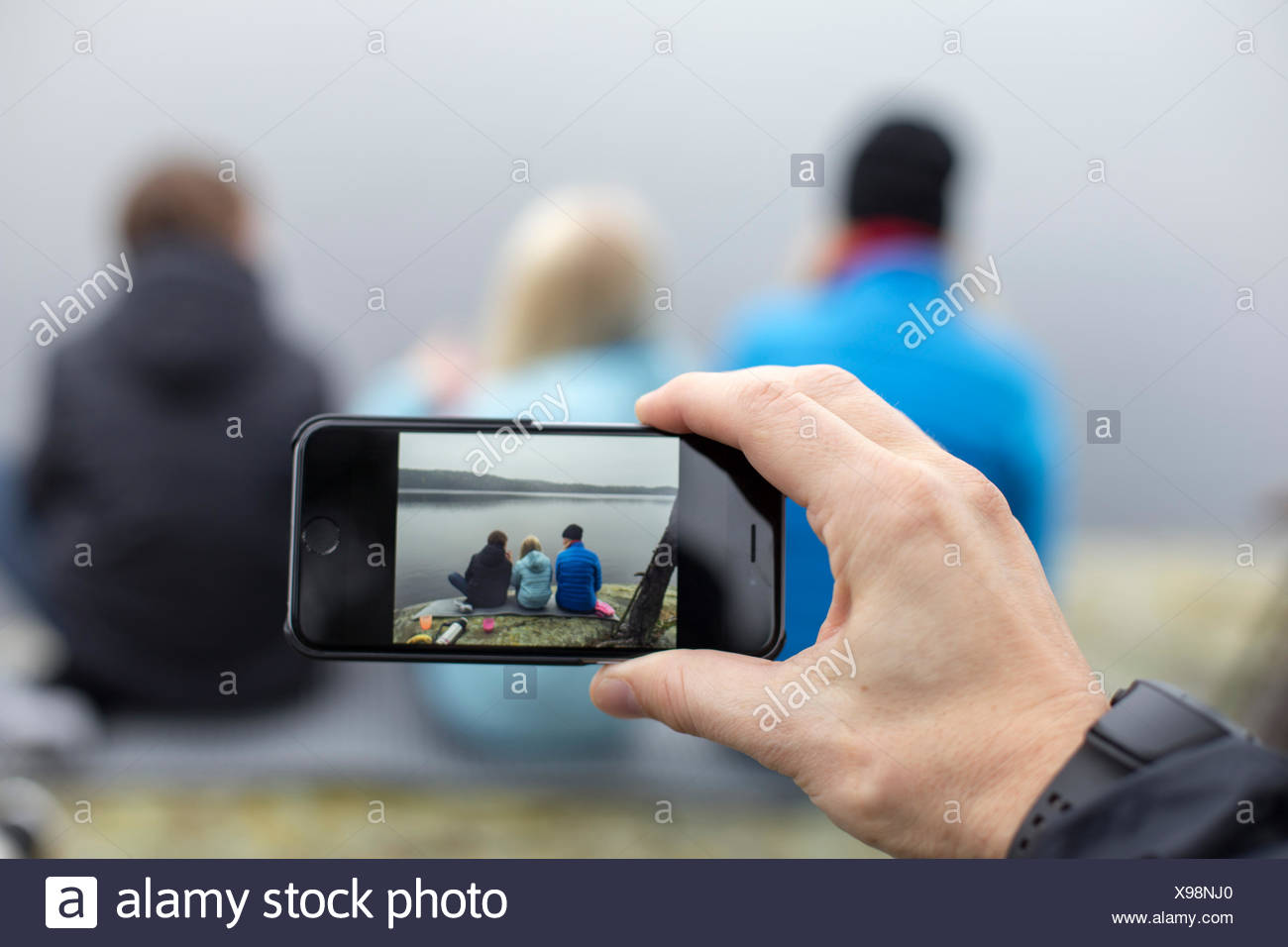 Suecia, Vastergotland, Lerum, Harsjon Harskogen, hombre, tomar la fotografía de una mujer con dos hijos (10-11, 12-13) con el smartphone Foto de stock