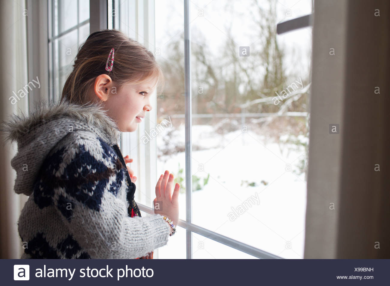 Niña mirando por la ventana al jardín de nieve Foto de stock