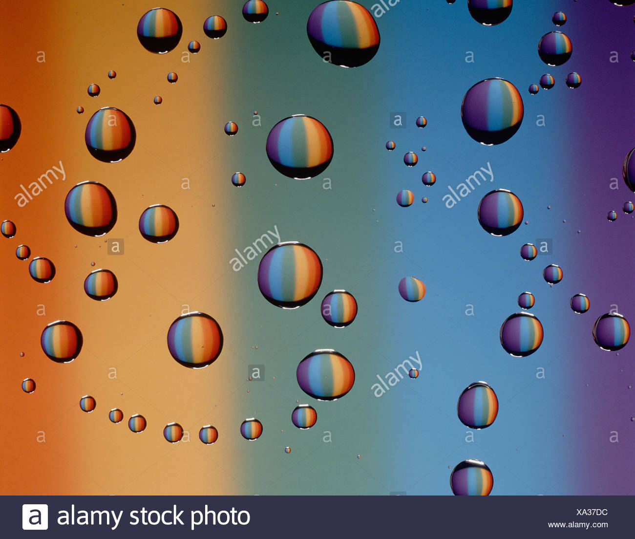 Sigue de cerca la vida de las gotas de agua sobre la superficie del cristal contra el telón de fondo de colores espectrales. Foto de stock