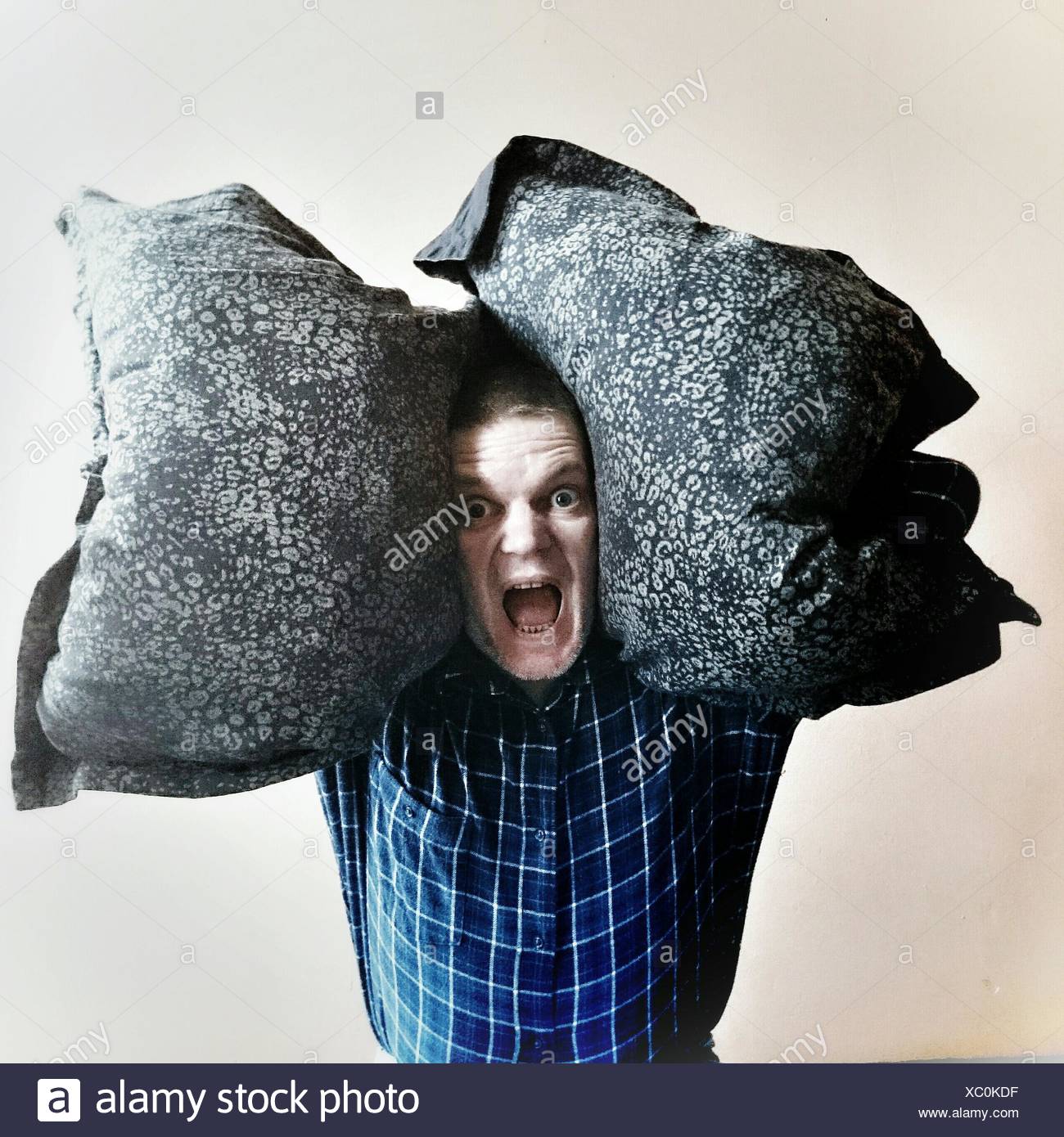 Retrato del hombre gritando mientras llevaba almohadas contra el fondo blanco. Foto de stock