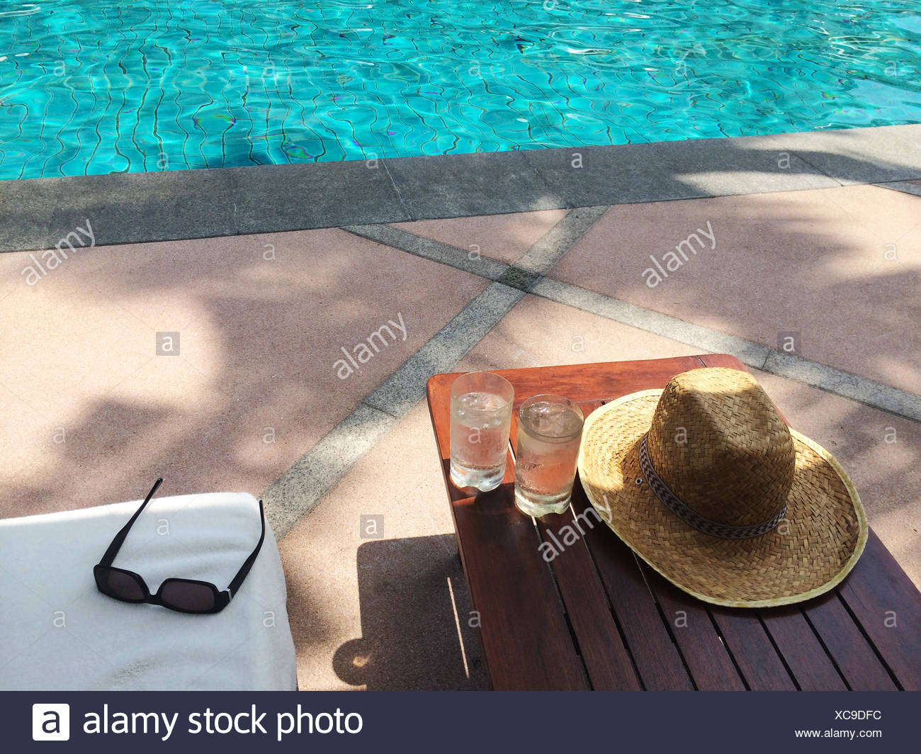 Paja sombrero para el sol, gafas de sol y dos vasos de agua de piscina Foto de stock