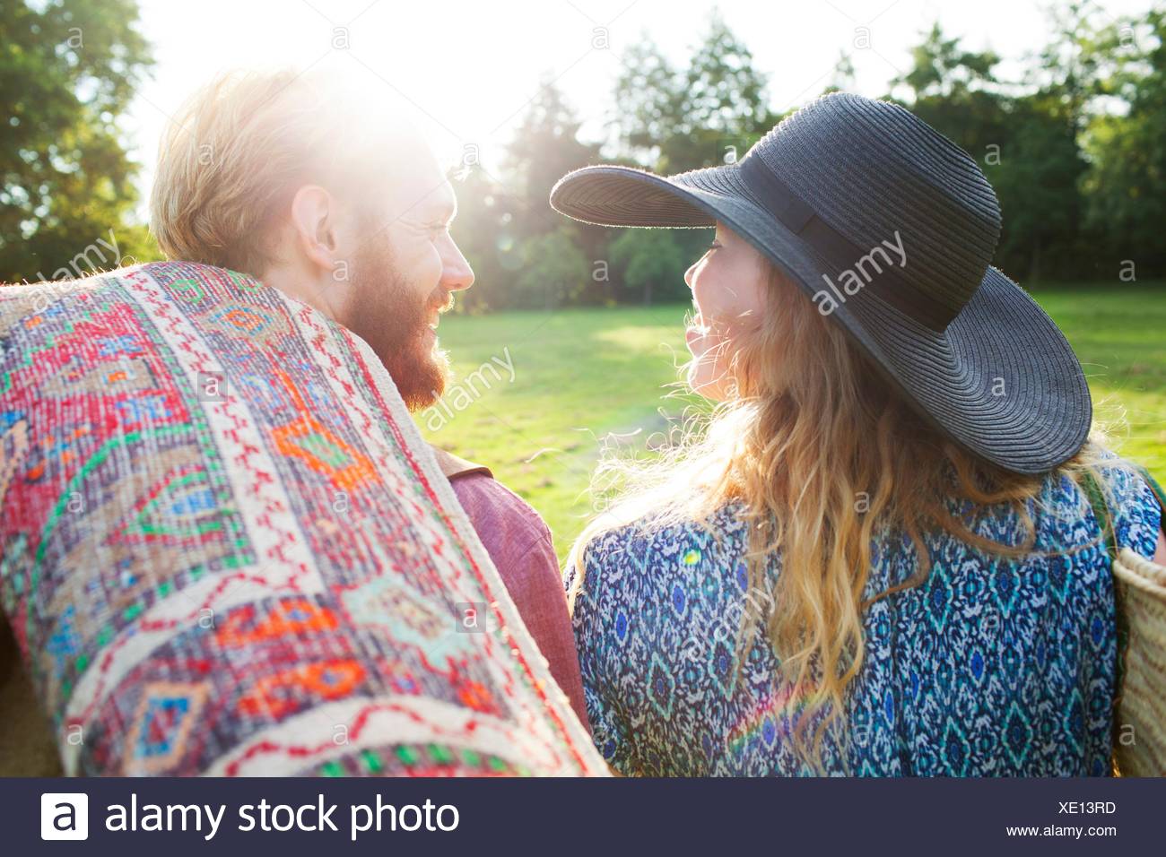 Vista trasera de la romántica pareja joven llevando la manta para picnic en el parque Foto de stock