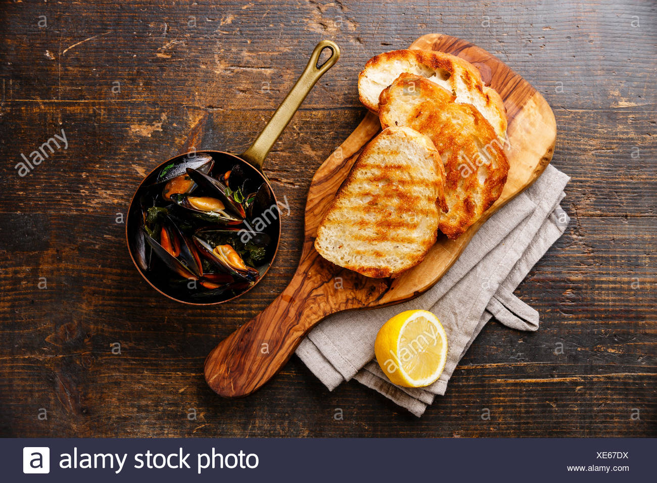 Mejillones en olla de cobre, tostadas de pan y limón sobre fondo de madera Foto de stock