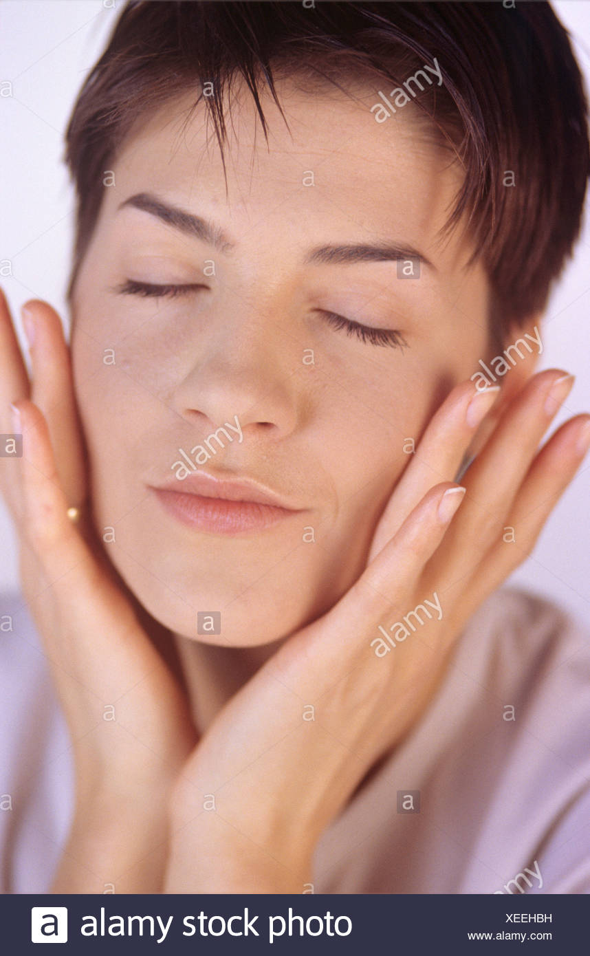 Hembra Morena Con Pelo Corto Los Ojos Cerrados Y Las Manos Sobre Las Mejillas Ahuecados Vistiendo Un Top Lila Pastel Fotografia De Stock Alamy