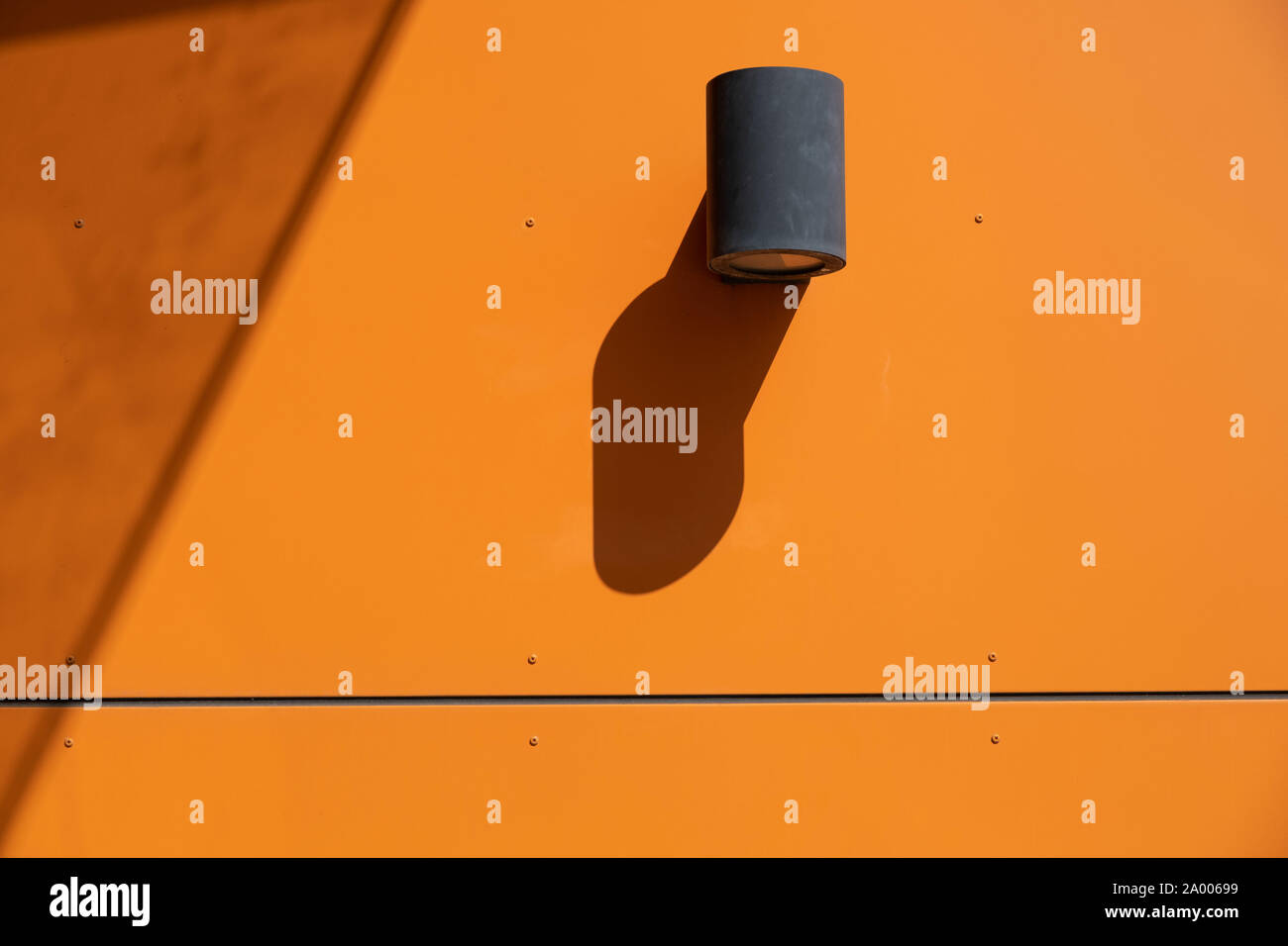 Lampe projecteur extérieur monté sur mur orange vif de bâtiment industriel à birght avec lumière du jour et d'ombre sévère copy space Banque D'Images