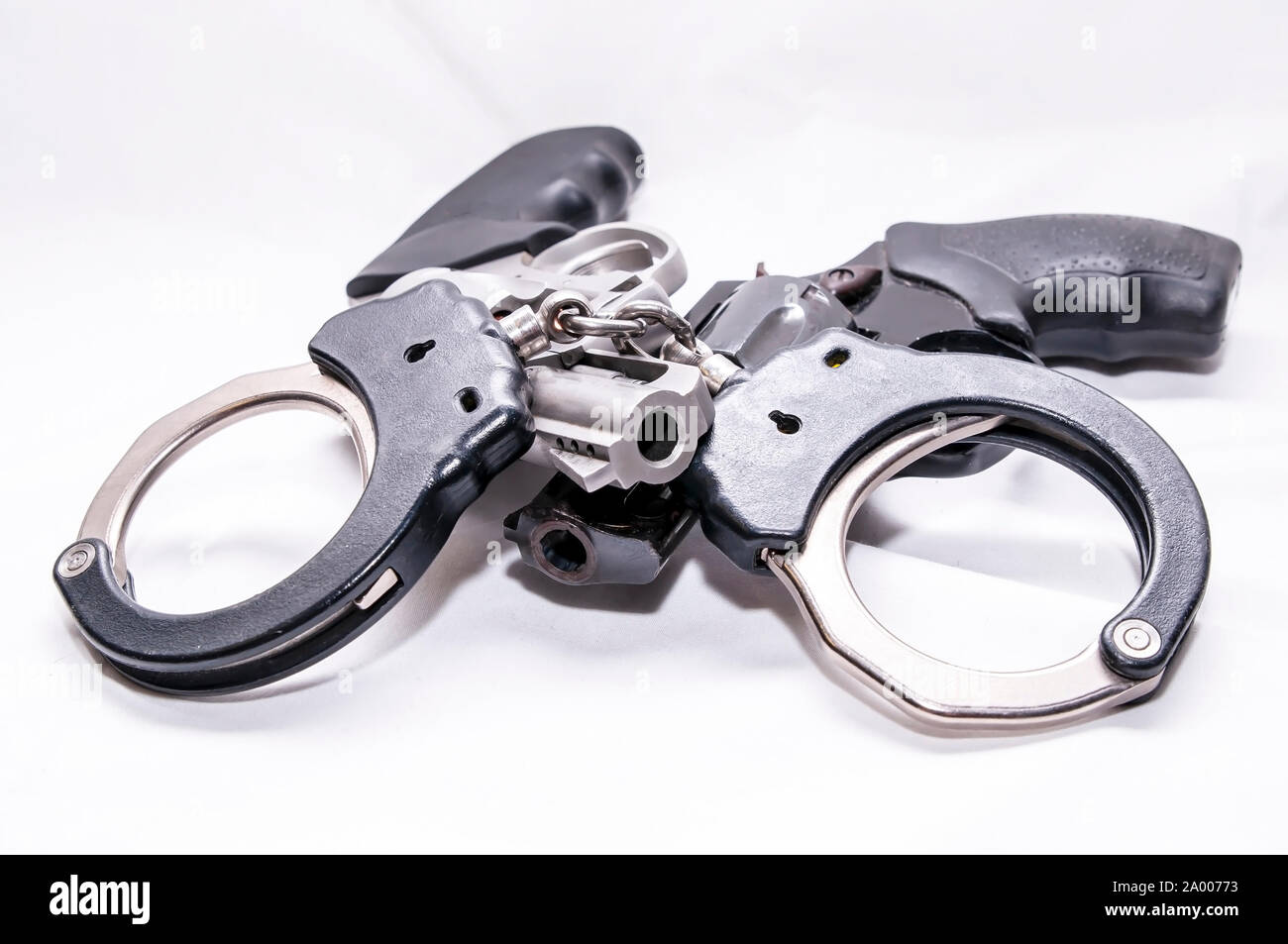 Un ensemble de deux tons de menottes en métal sur le dessus de deux revolvers, une noire et l'autre l'acier inoxydable sur un fond blanc Banque D'Images