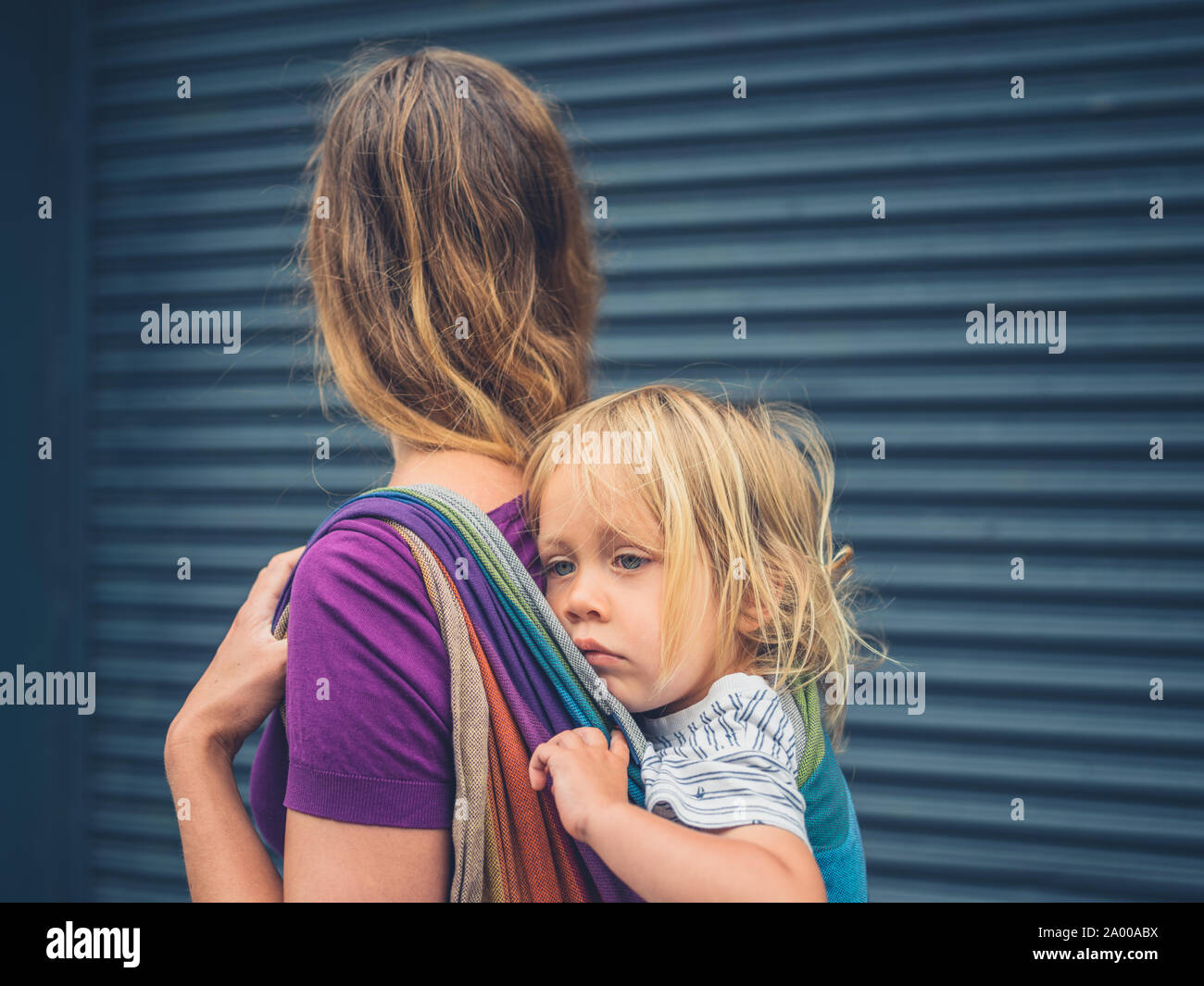 Une jeune mère millénaire est de marcher dans la rue avec son enfant attaché  sur son dos dans une écharpe Photo Stock - Alamy