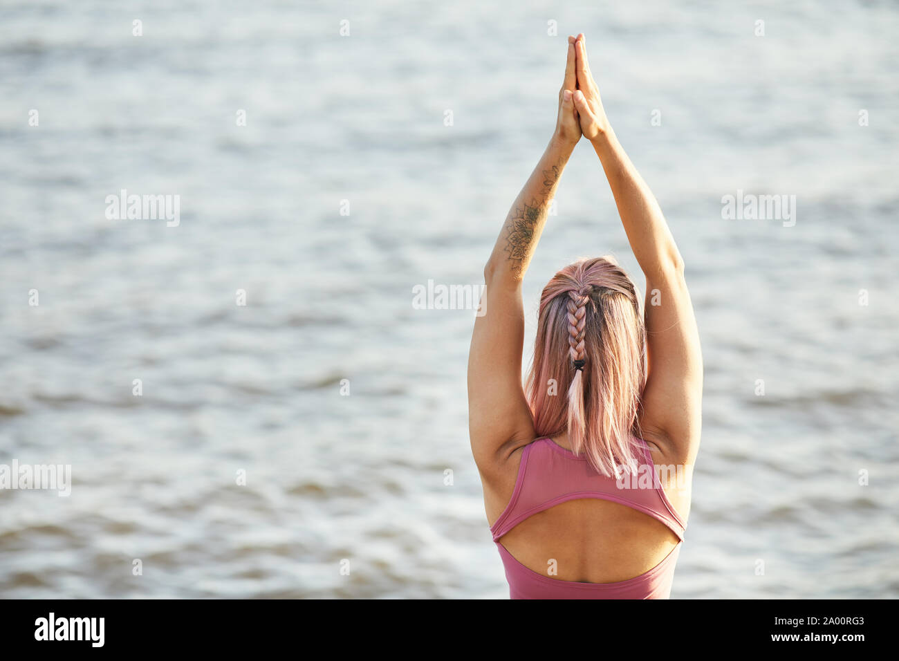Vue arrière du jeune femme aux cheveux blonds leva son bras et méditer en regardant la mer en plein air Banque D'Images