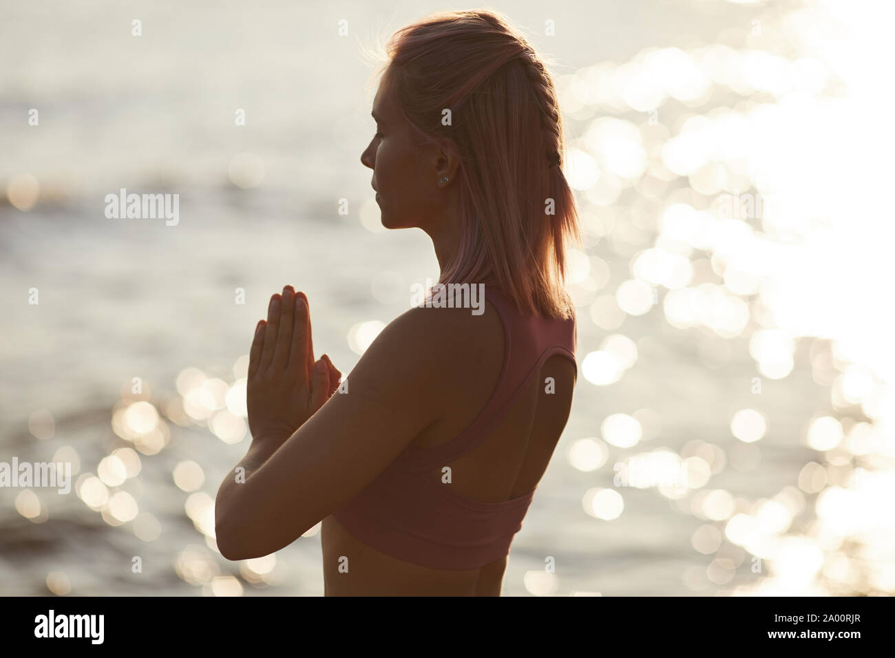 Vue arrière du jeune femme aux cheveux blonds debout avec les yeux fermés et méditant contre la belle mer en plein air Banque D'Images