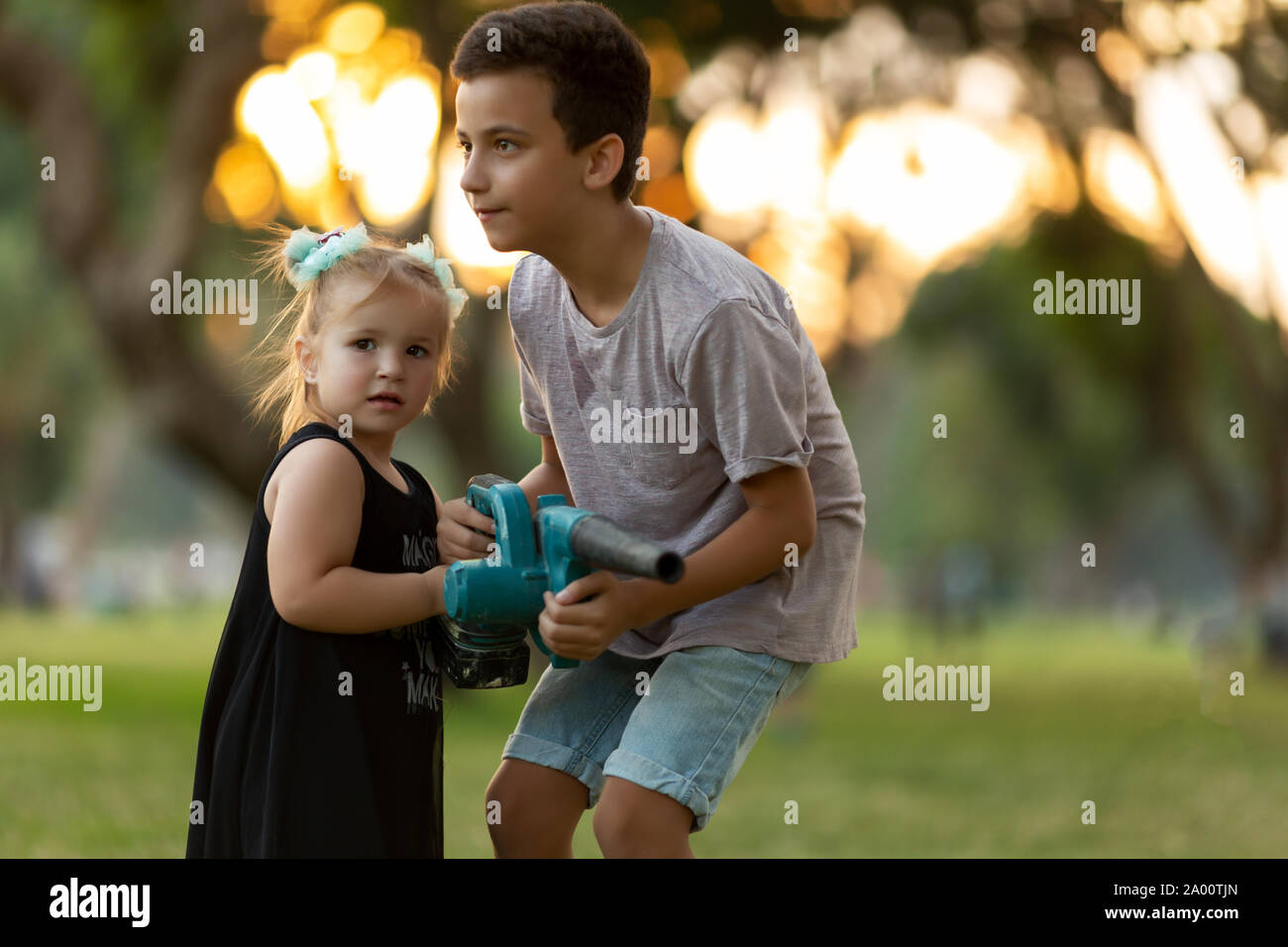 Les enfants jouent avec les feuilles tombées de nettoyage d'un souffleur dans un parc de la ville d'automne Banque D'Images