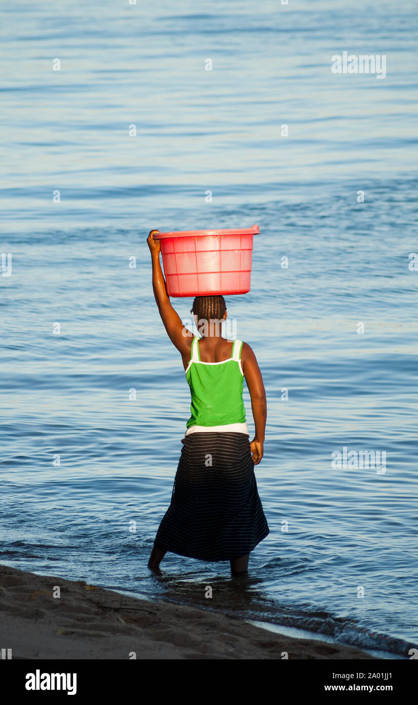 Une jeune fille sur la rive du lac Malawi porte un panier sur la tête. Banque D'Images