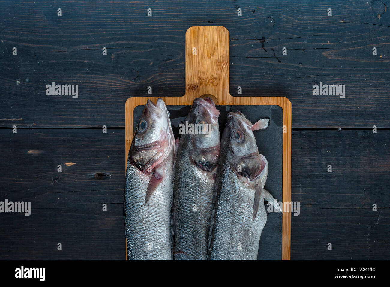 Poissons de mer frais sur une planche à découper sur une table en bois foncé Banque D'Images